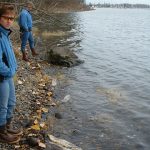 two people on river bank viewing two dead spawned fish