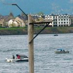 Bird nesting platform on pole next to river with several boats in river