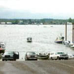 Boat ramp with several vehicle backing boats into river and pulling boats out out of river