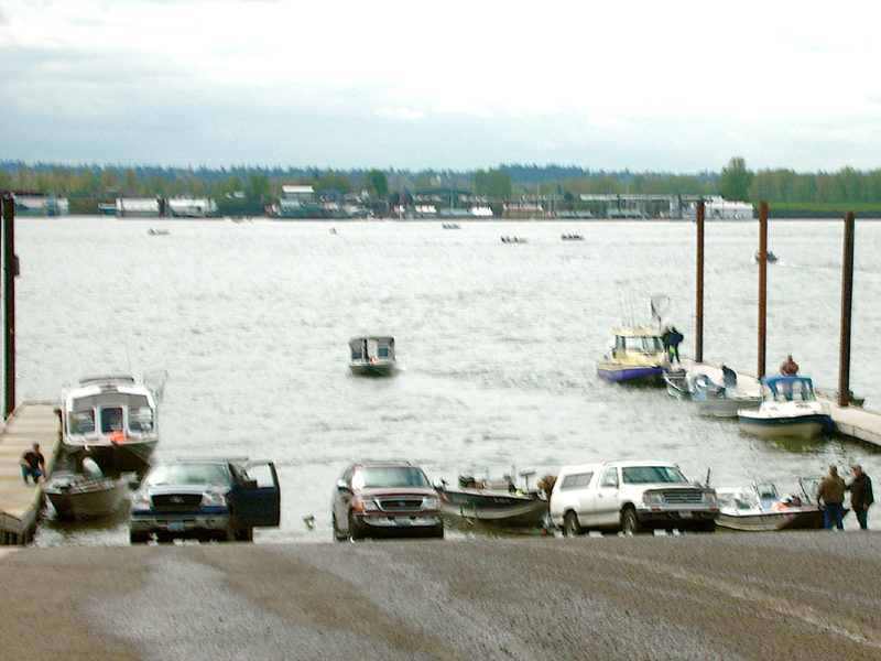 Boat ramp with several vehicle backing boats into river and pulling boats out out of river