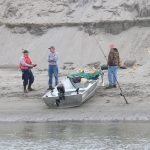 Three people on river bank next to boat